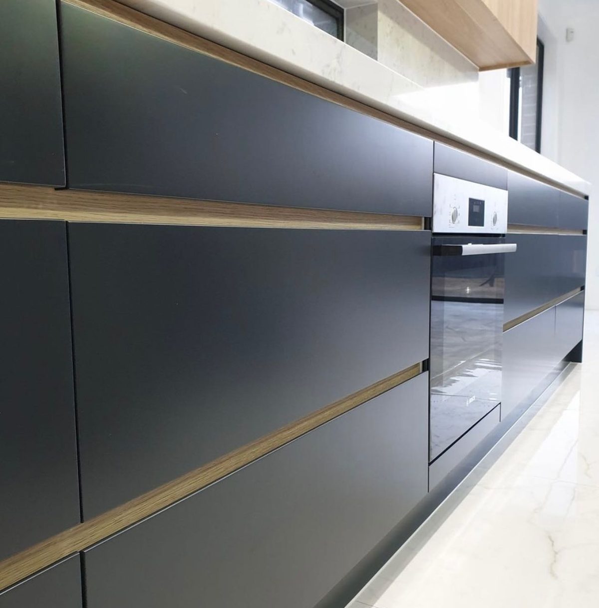 Close-up of matte charcoal cabinetry with a natural oak inlay strip and an integrated stainless oven, showcasing FD Joinery's cabinetry detailing.