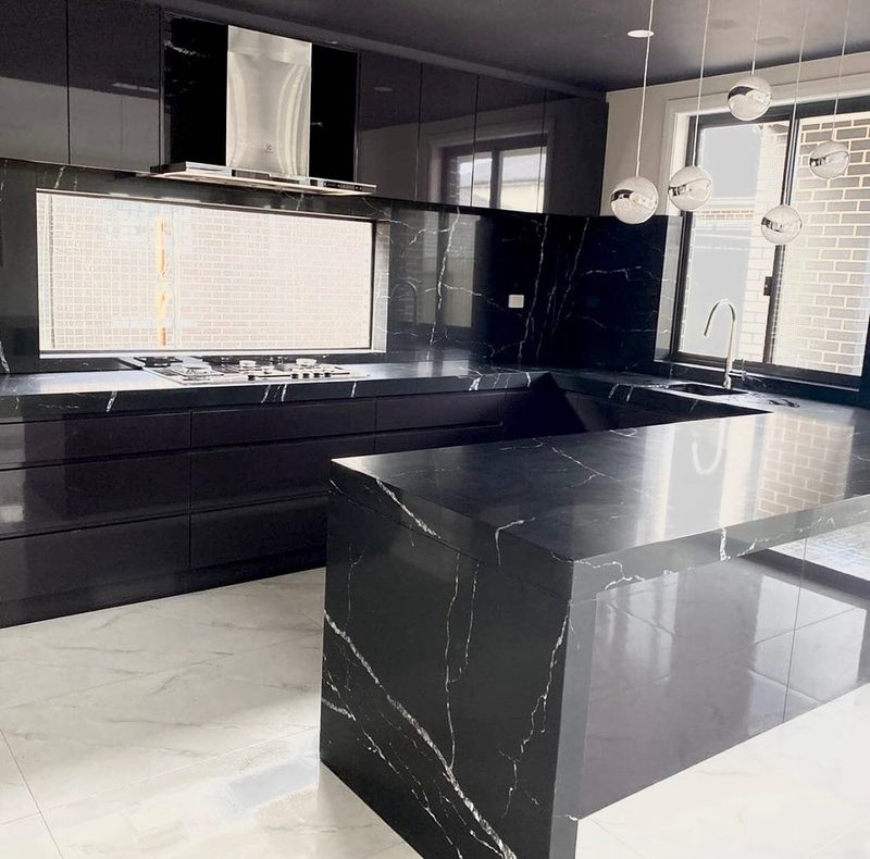 Glossy black marble waterfall island bench with matching splashback and sphere pendant lighting in an all-black kitchen.