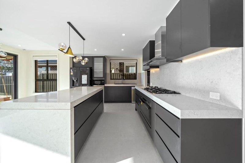 Charcoal grey kitchen with a white quartz waterfall island bench, integrated rangehood and warm under-cabinet lighting.