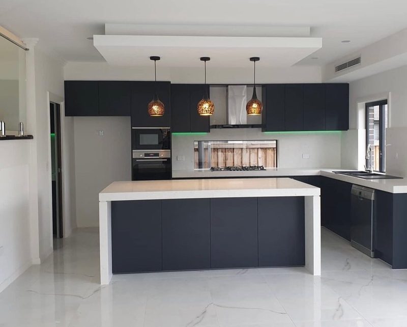 Matte navy kitchen with a white quartz island bench, three woven pendant lights and integrated green under-cabinet lighting.