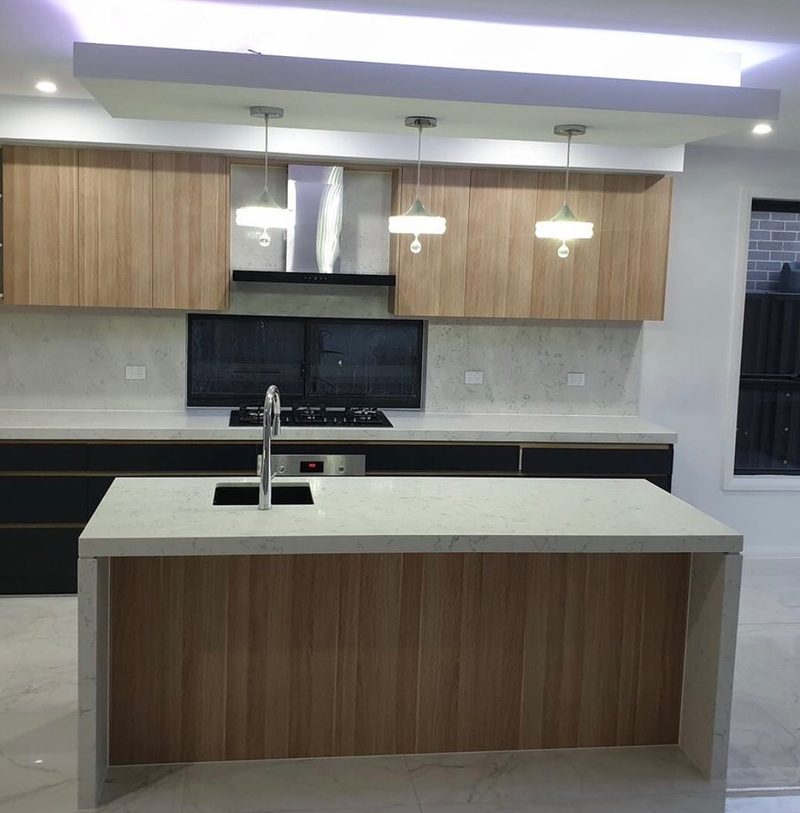 Light oak-grain kitchen with a white quartz waterfall island bench and three drop pendant lights.