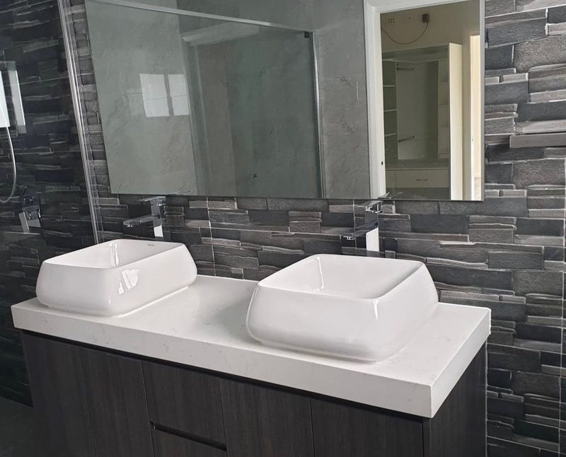 Dark timber double vanity with square vessel basins set against a textured charcoal stone feature wall.
