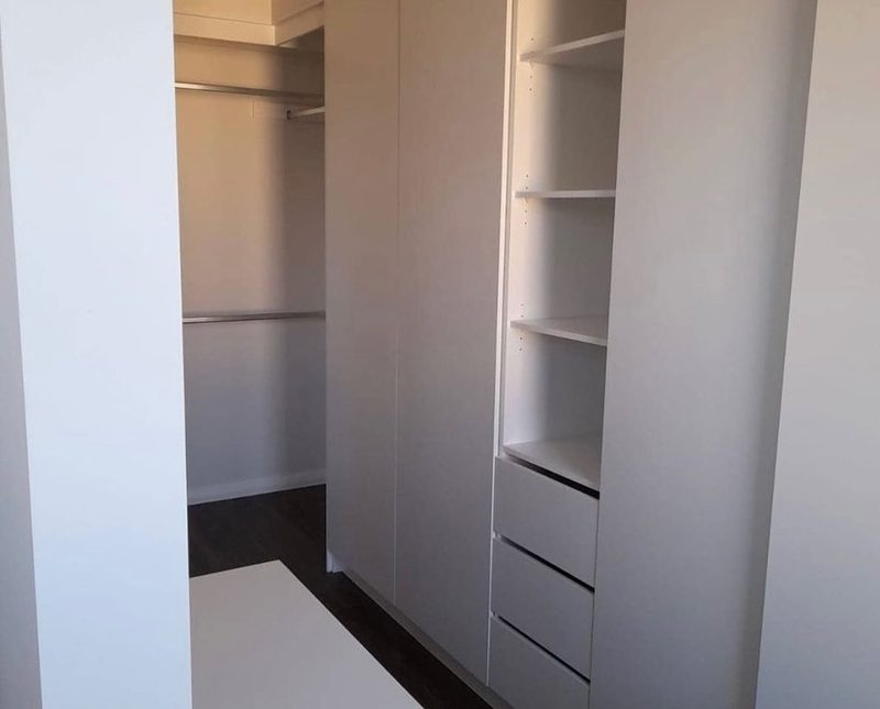White walk-in wardrobe with adjustable shelving, hanging rails and a bank of soft-close drawers.