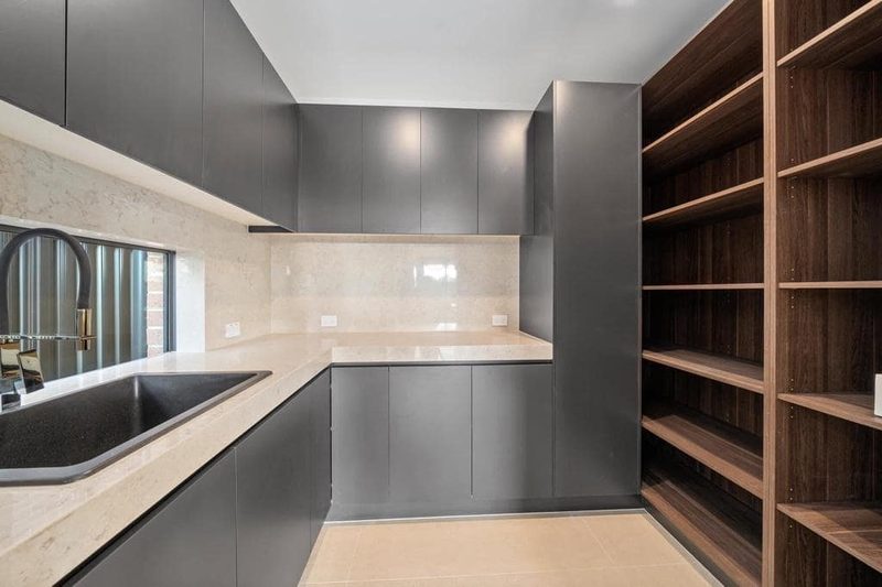 Butler's pantry with open walnut shelving, matte charcoal cabinetry and a brass gooseneck tap.