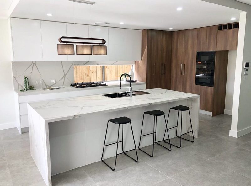 White quartz waterfall island with dark walnut cabinetry and black bar stools in an open-plan kitchen.